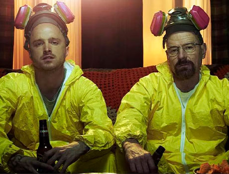 Imagen de Jesse Pinkman y Walter White sentados en un sofá con un traje de aislamiento amarillo y unas máscaras de gas en la cabeza en la serie Breaking Bad.