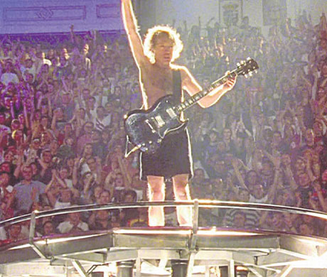 Fotografía de Angus Young en su pose icónico encima de un podio en un concierto de ACDC.